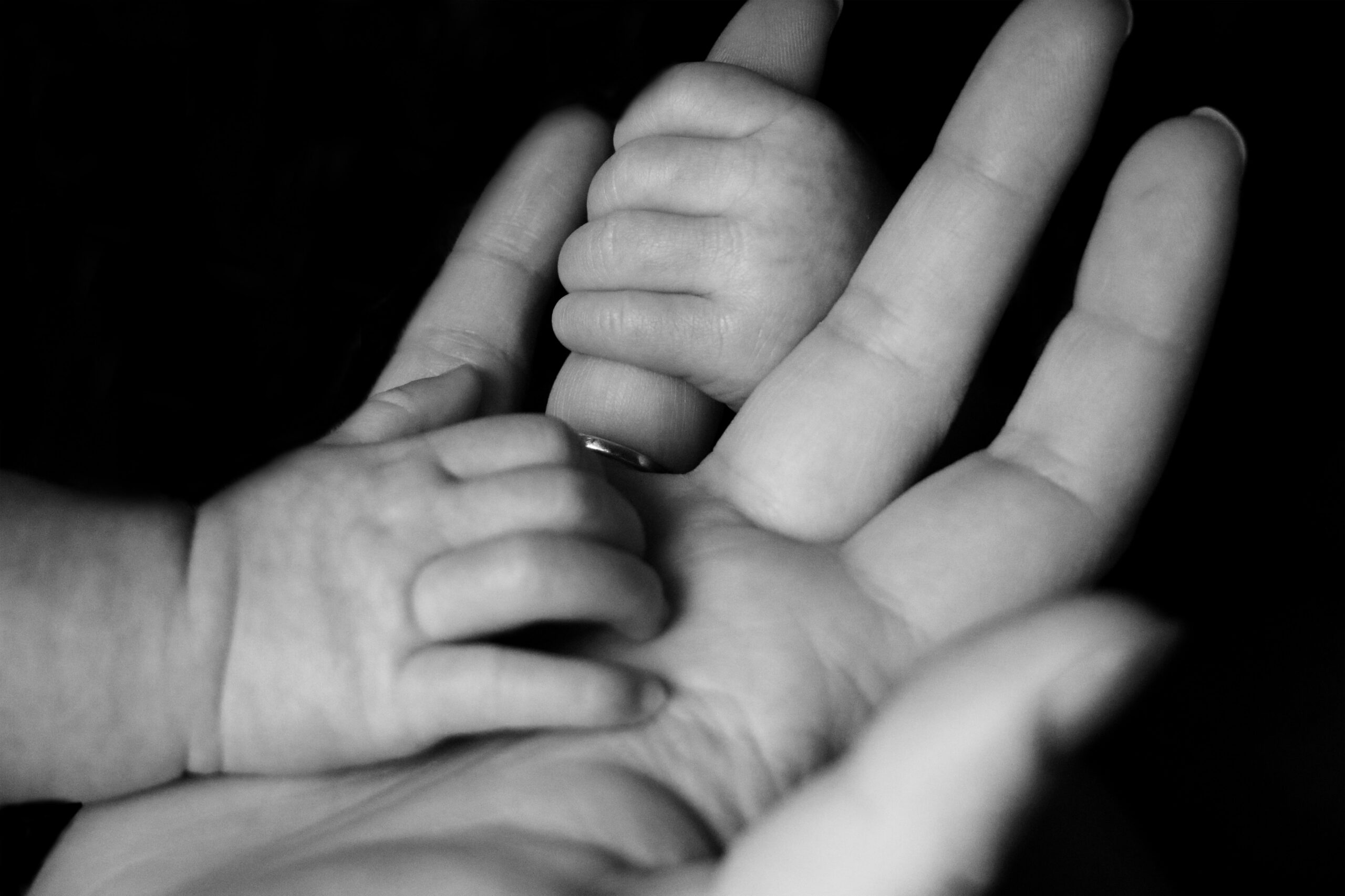 Black and white photo of an adult holding a baby's hand. It's presumed that the parent is wondering if addiction is hereditary.