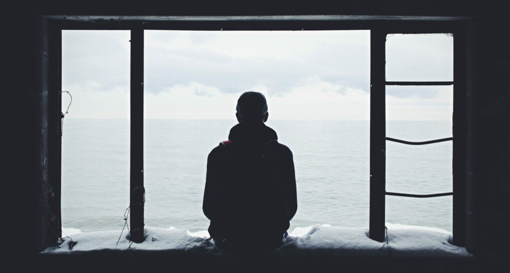 A man sits in front of an open window to represent the signs of high-functioning depression
