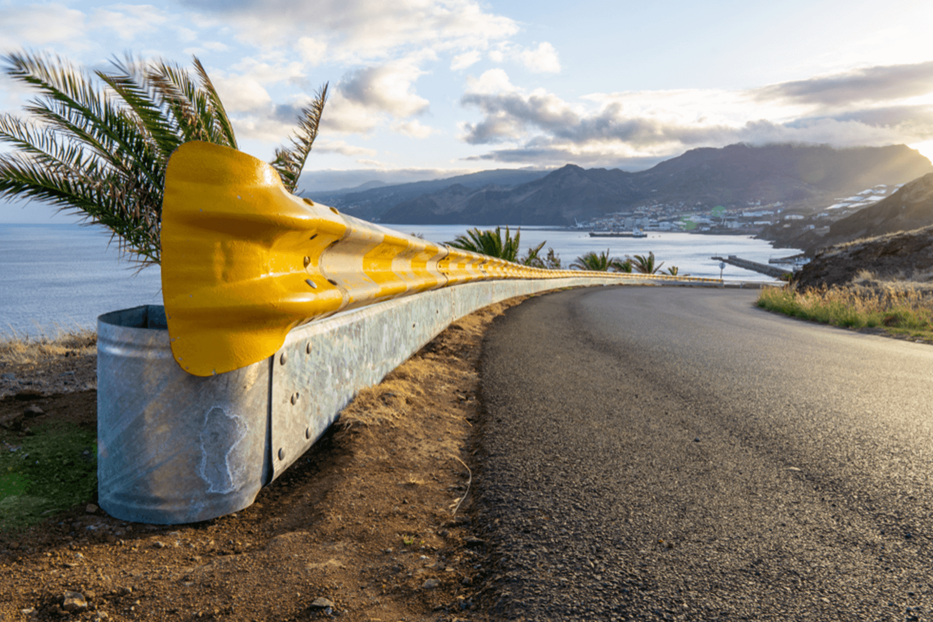 Yellow guardrail along curvy road with sunset over the sea and village
