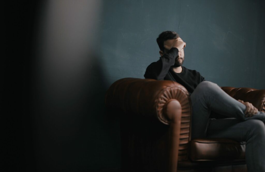 A man sits on a couch with his hand on his head to represent Percocet withdrawal symptoms.