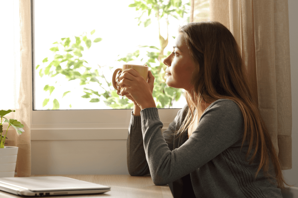 a woman is looking out a window while drinking coffee to represent alcohol stimulant effects. 