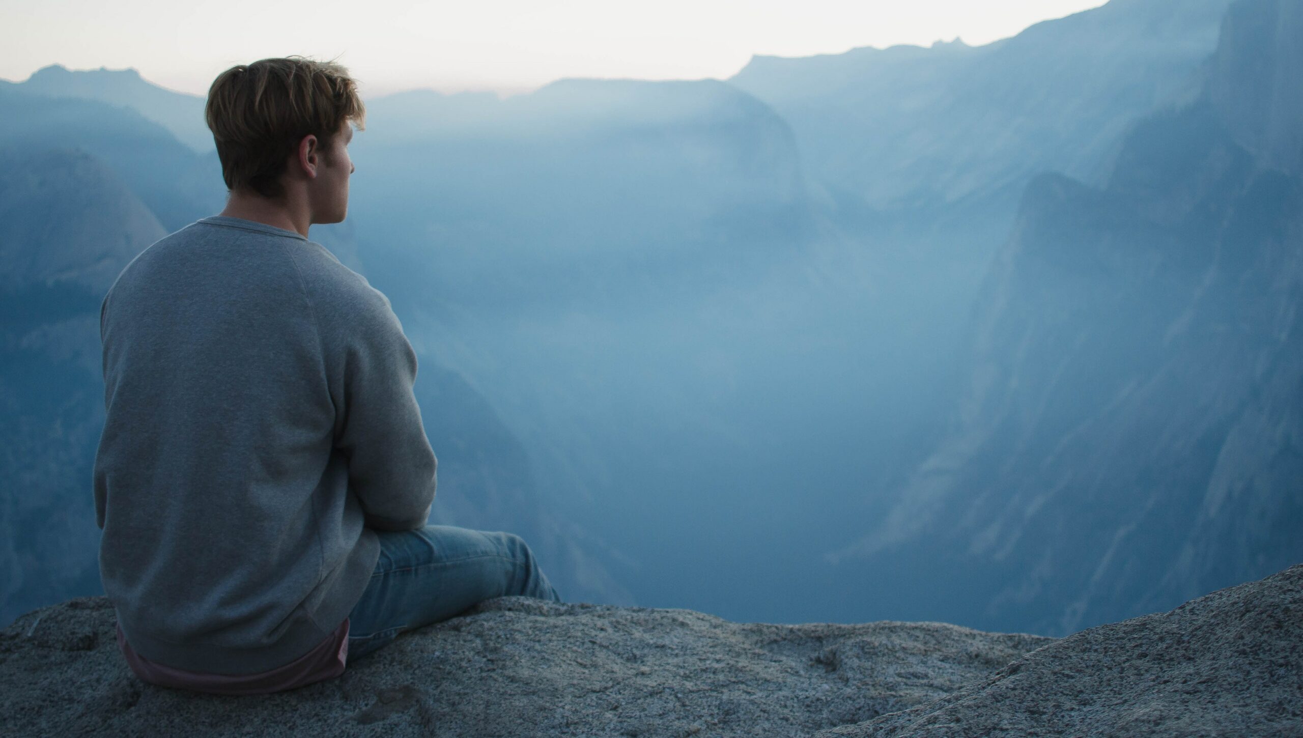 A man is sitting looking out at a mountain range to represent wondering, "how does a vivitrol shot work?".