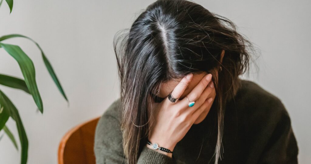 A woman sits with her hand on her head to represent cocaine detox symptoms.