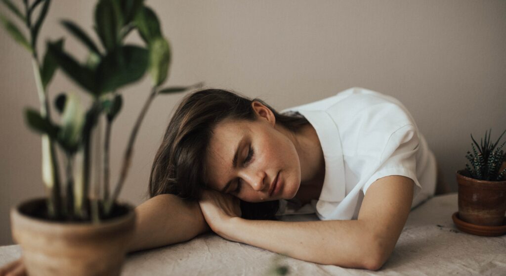 A woman rests her head on a table to represent heroin withdrawal symptoms.