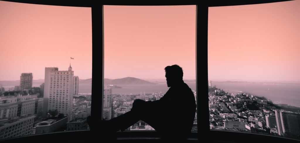 Man looks out window to represent getting drunk alone