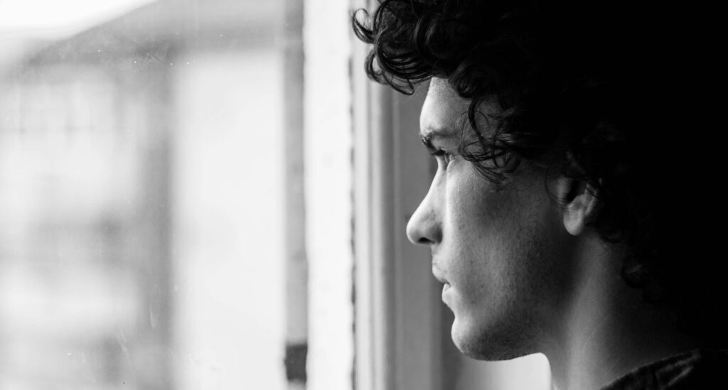 A man looks out a window looking concerned to represent how long is alcohol treatment. 