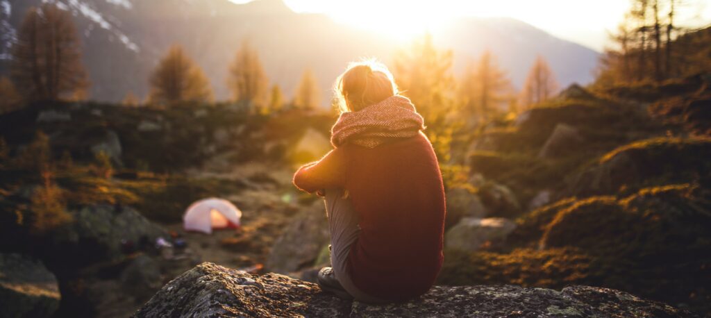 A woman sits on a hillside at sunset to represent drug half life