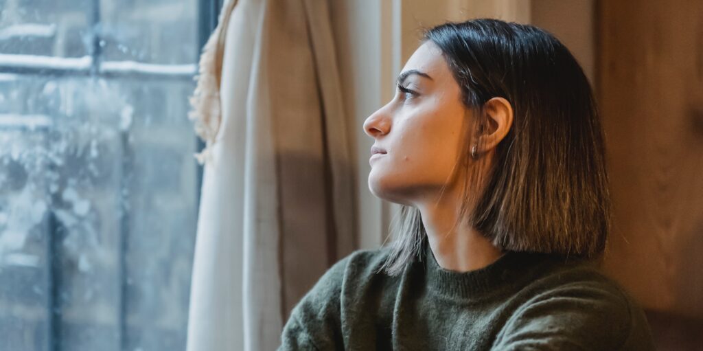 a woman looks out a window to represent the question: is xanax considered an opioid?