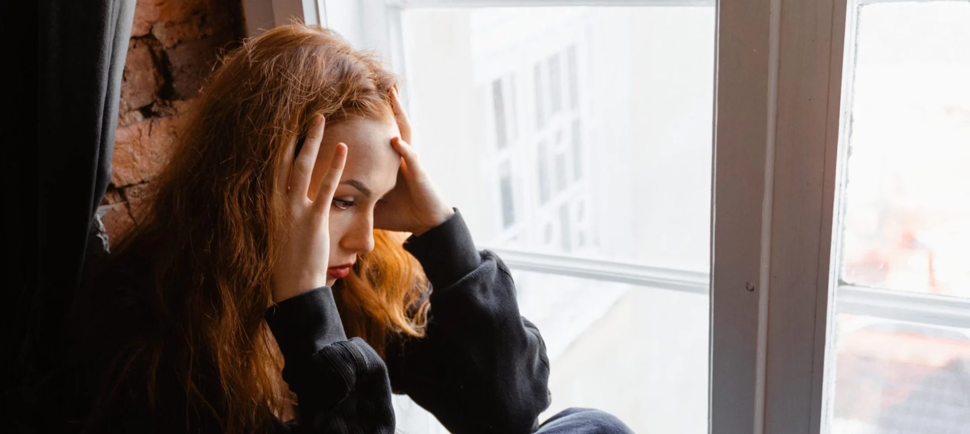 A woman sits with her hands on her head to represent substance abuse relapse.
