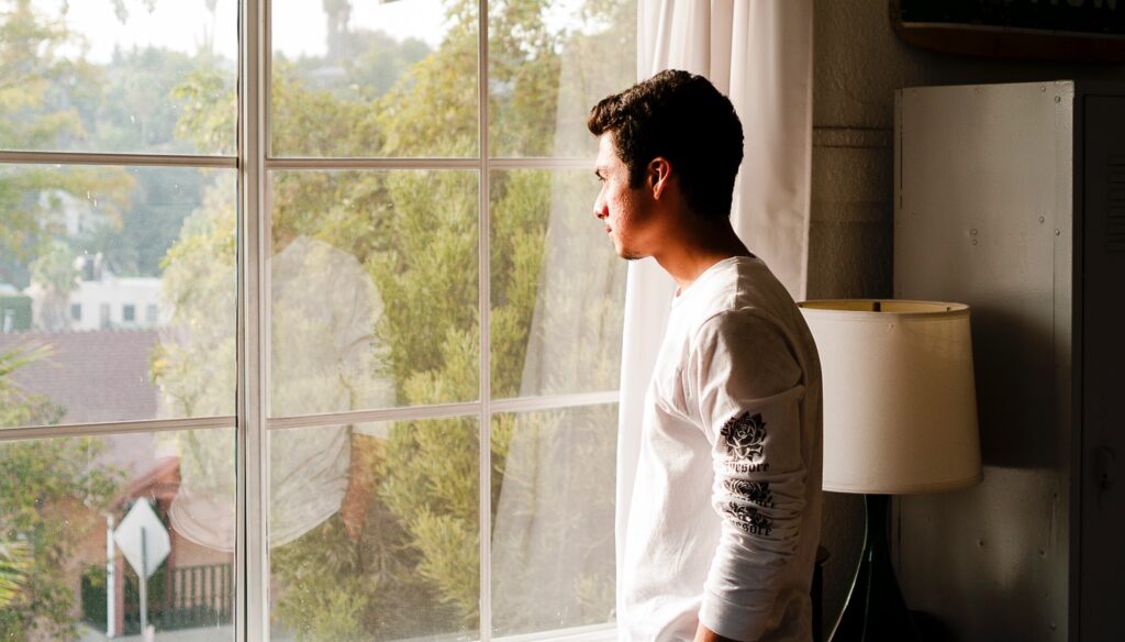 A man looks out a window representing Polysubstance abuse disorder. 
