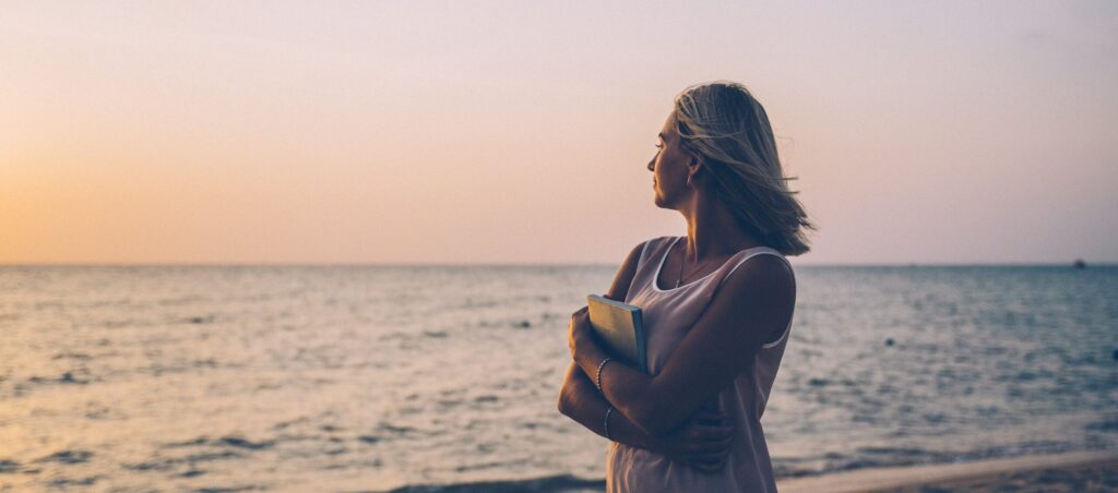 A woman walks the beach at sunset after learning about signs your liver is healing